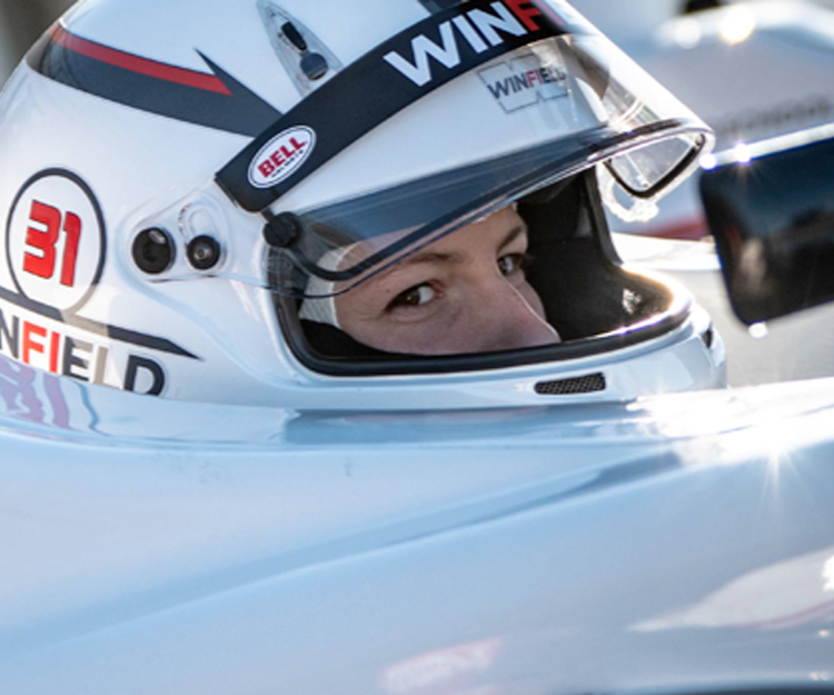 A woman with a WIM racing helmet in a racecar.