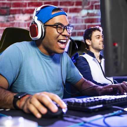 Two men sit by a desk gaming on their computers