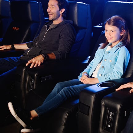 A girl and her father sit in D-BOX cinema seats